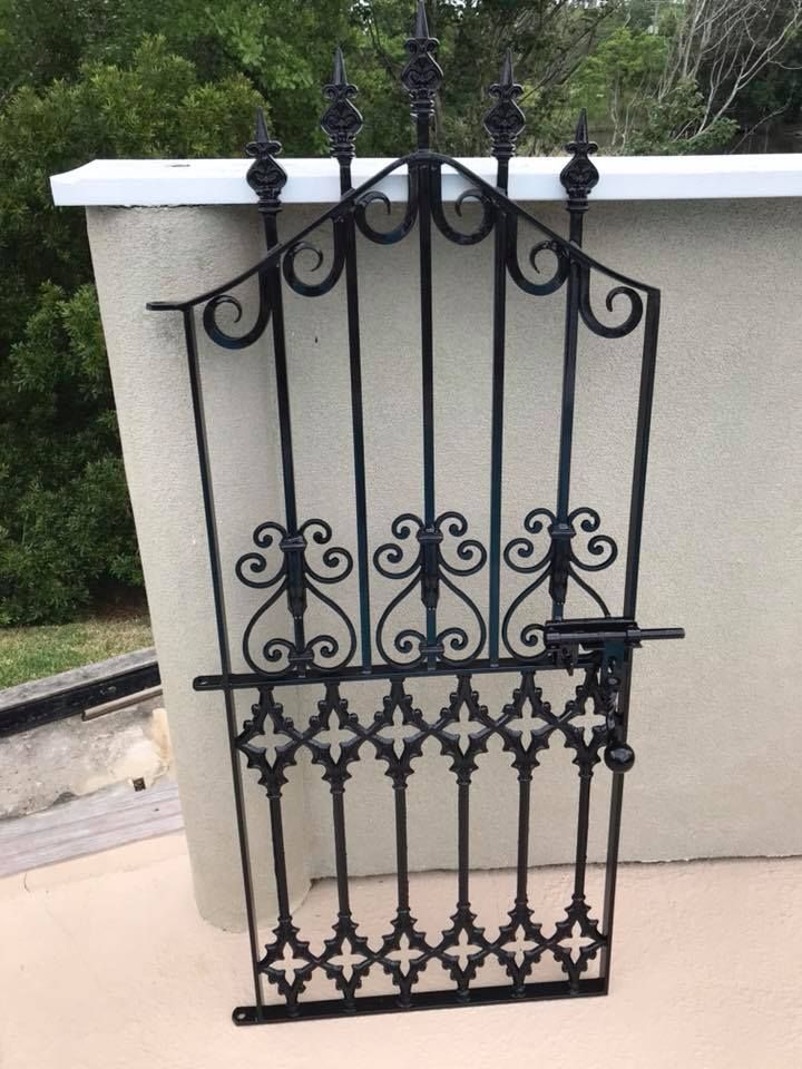 Black wrought-iron decorative gate leaning against a beige wall outdoors.