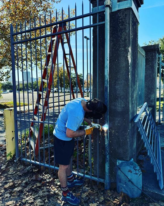 Worker using tools to repair a metal fence beside a concrete gate pillar outdoors