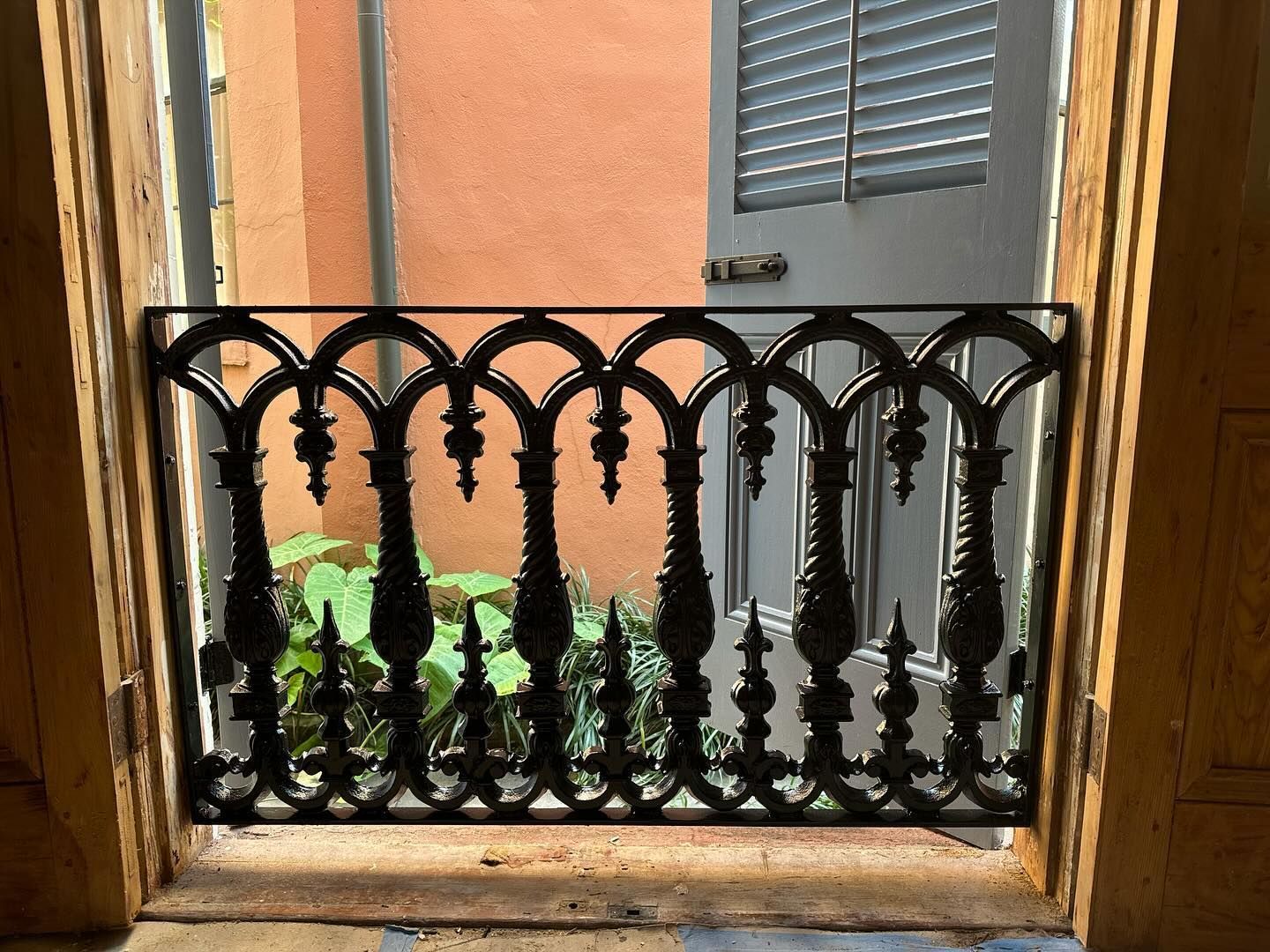 Black wrought-iron balcony railing against an orange wall with a small green plant outside the doorway