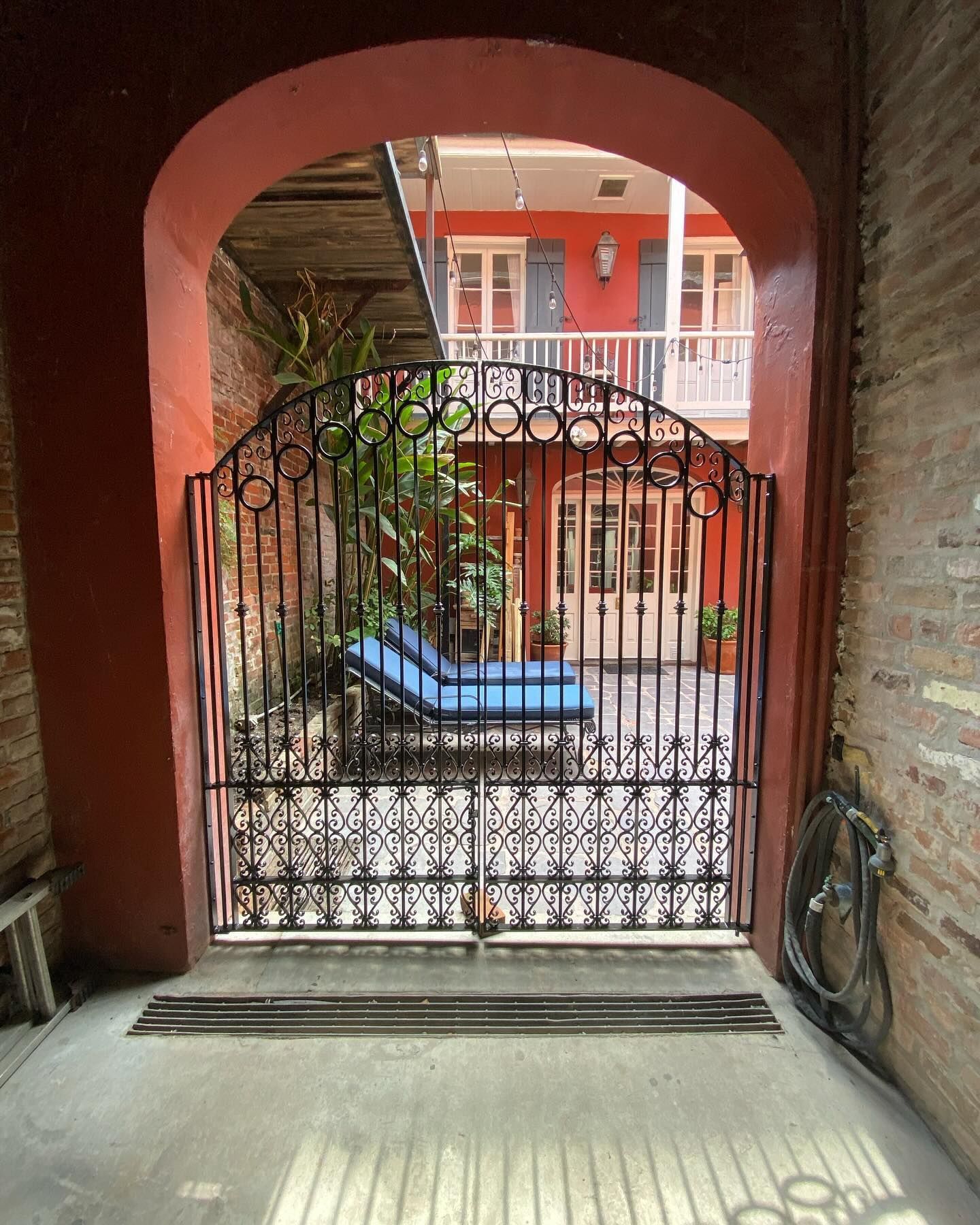 Wrought-iron gate in a red archway opening to a courtyard with potted plants and a blue bench