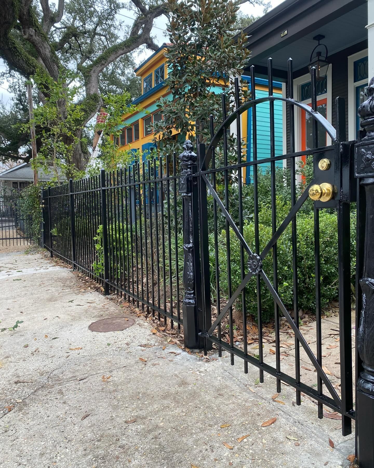 Black wrought-iron fence along a gravel path beside a colorful house and trees