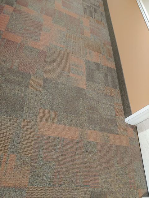Brown patterned carpet with peach accents near a beige wall and white trim.