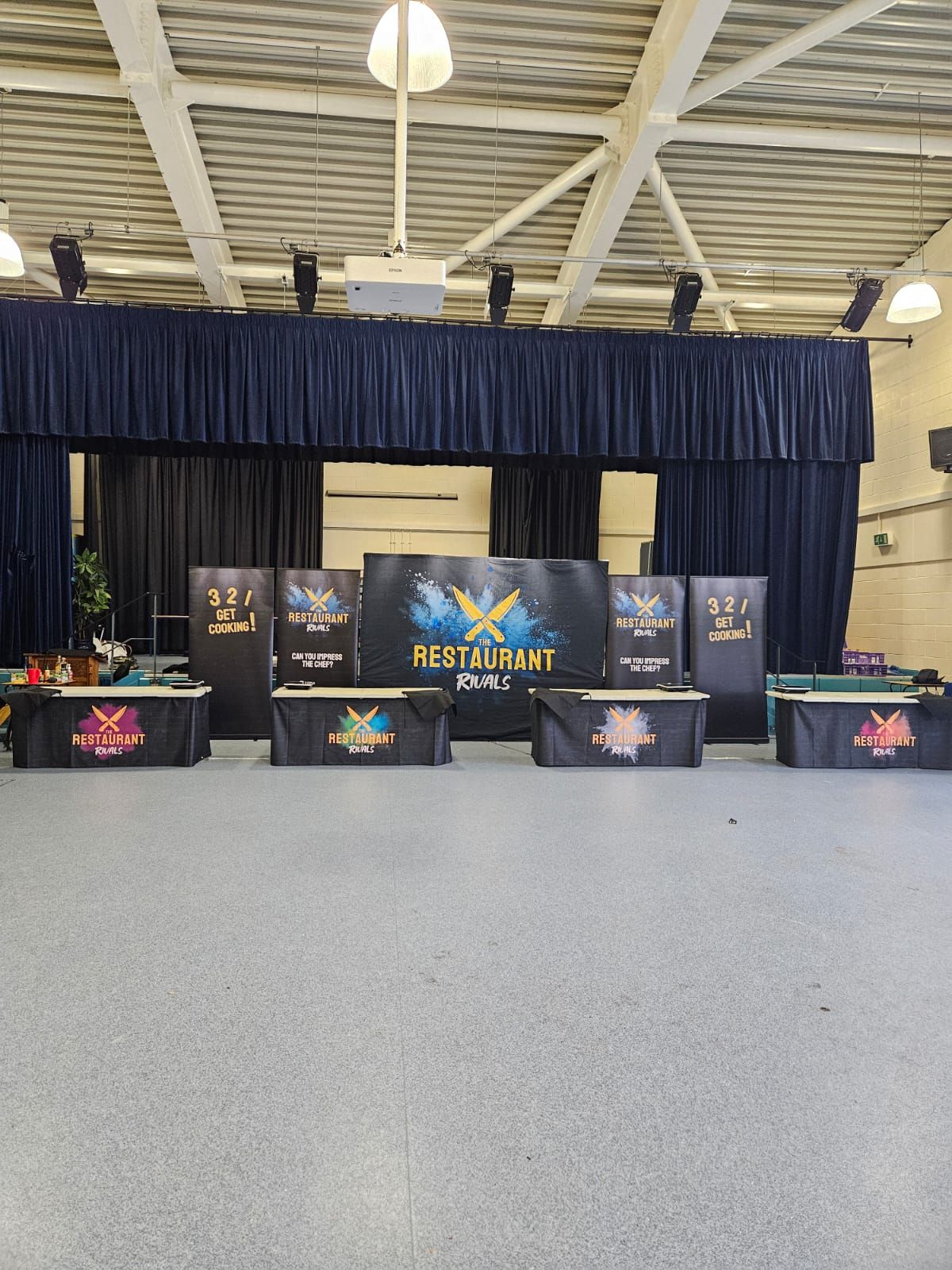 Stage set with black backdrop, banners, and tables for an event; the floor is grey.