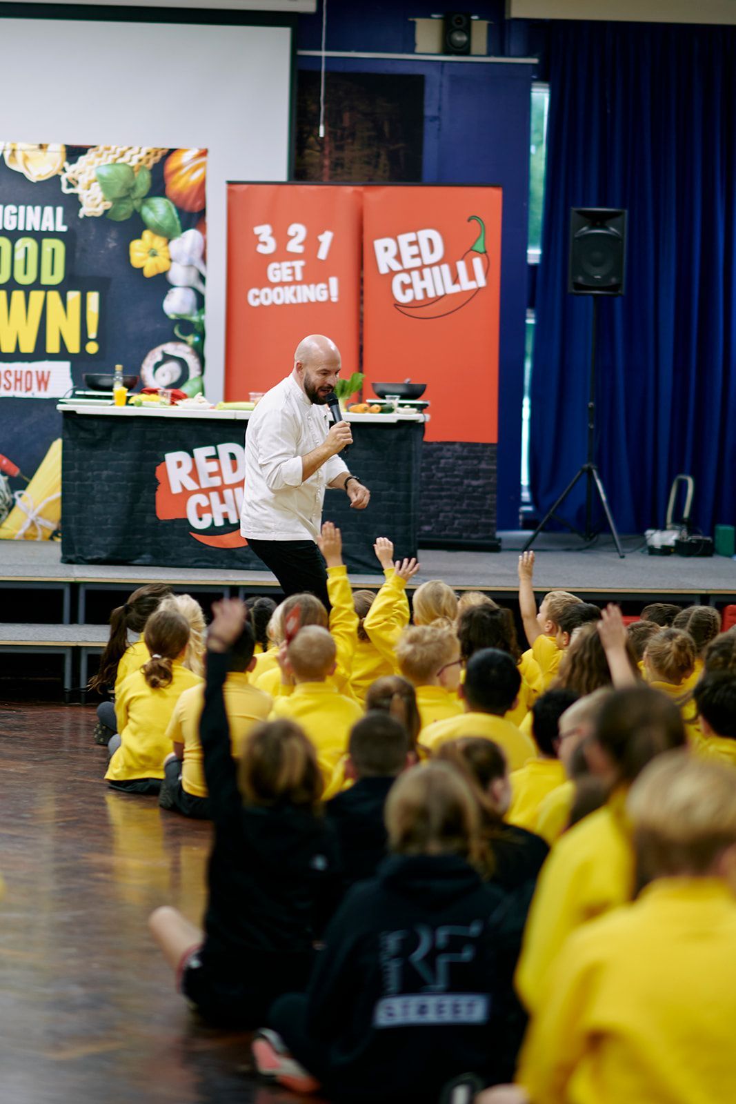 Chef speaking to children sitting on floor; red chili banner visible.