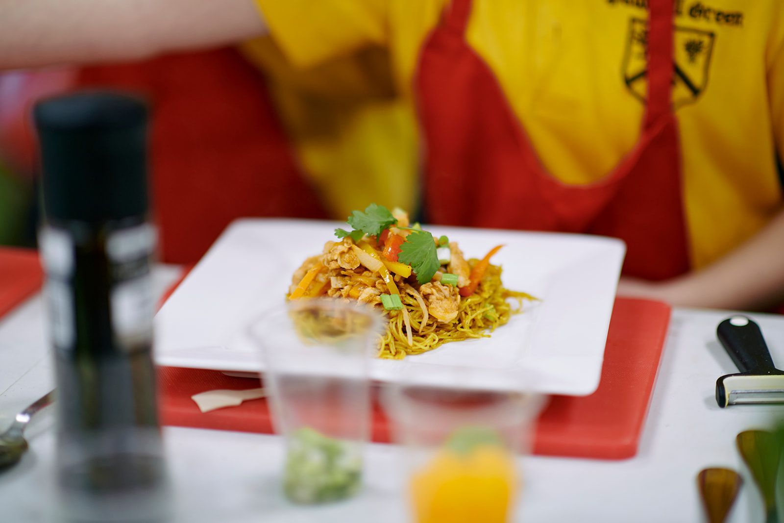 Plate of food with vegetables and herbs, red apron in background.