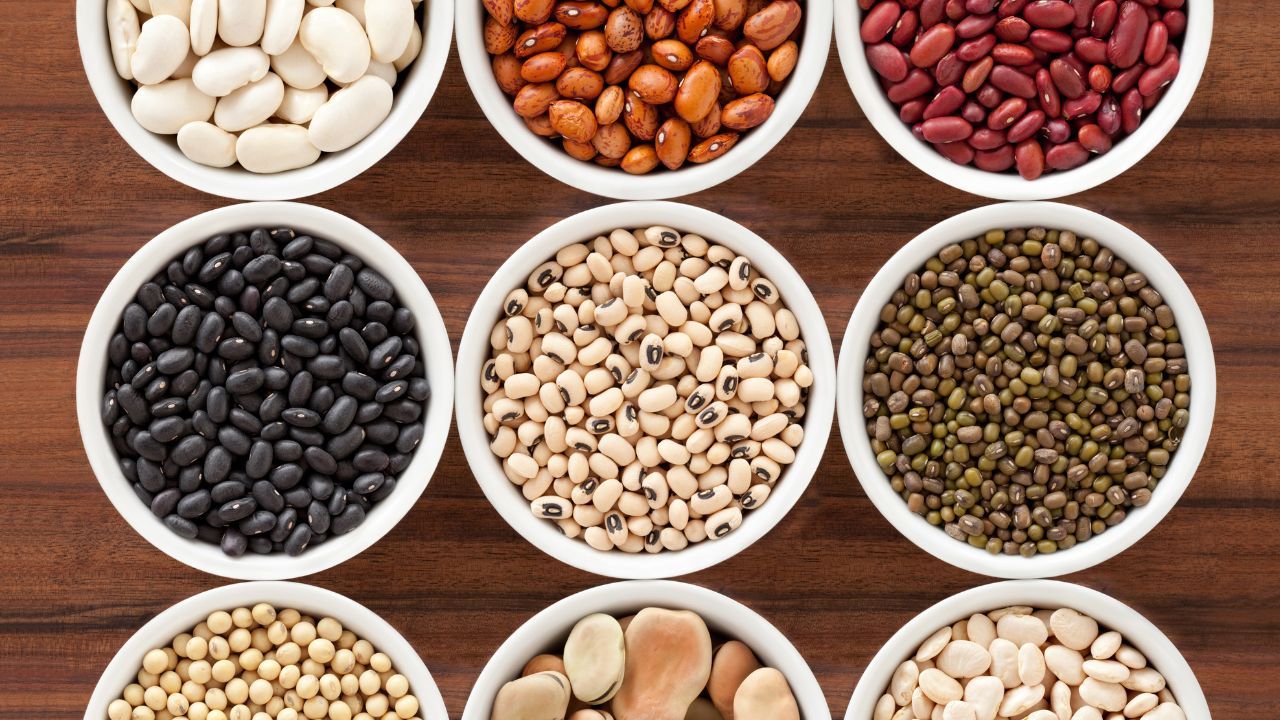 Nine white bowls filled with various dried beans, arranged in a grid, on a wooden surface.