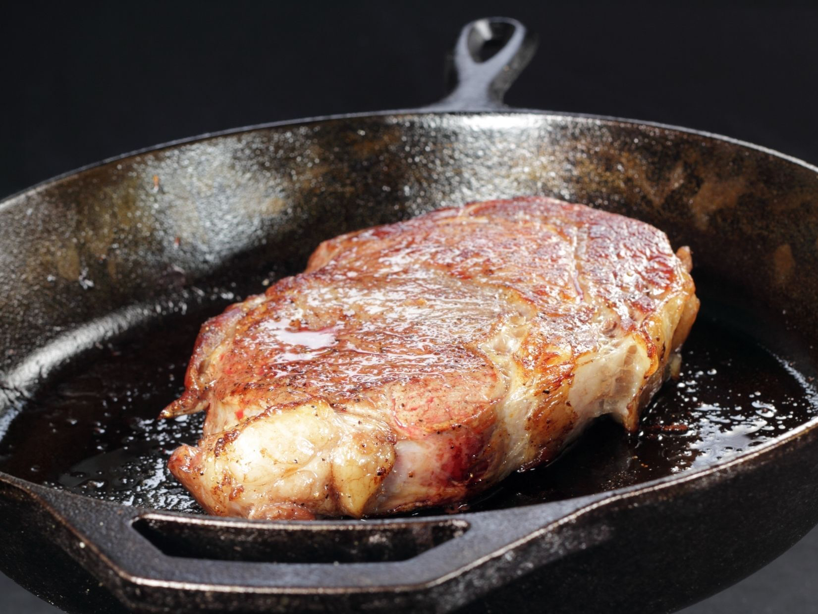 Seared steak in a cast iron skillet, with a dark background.