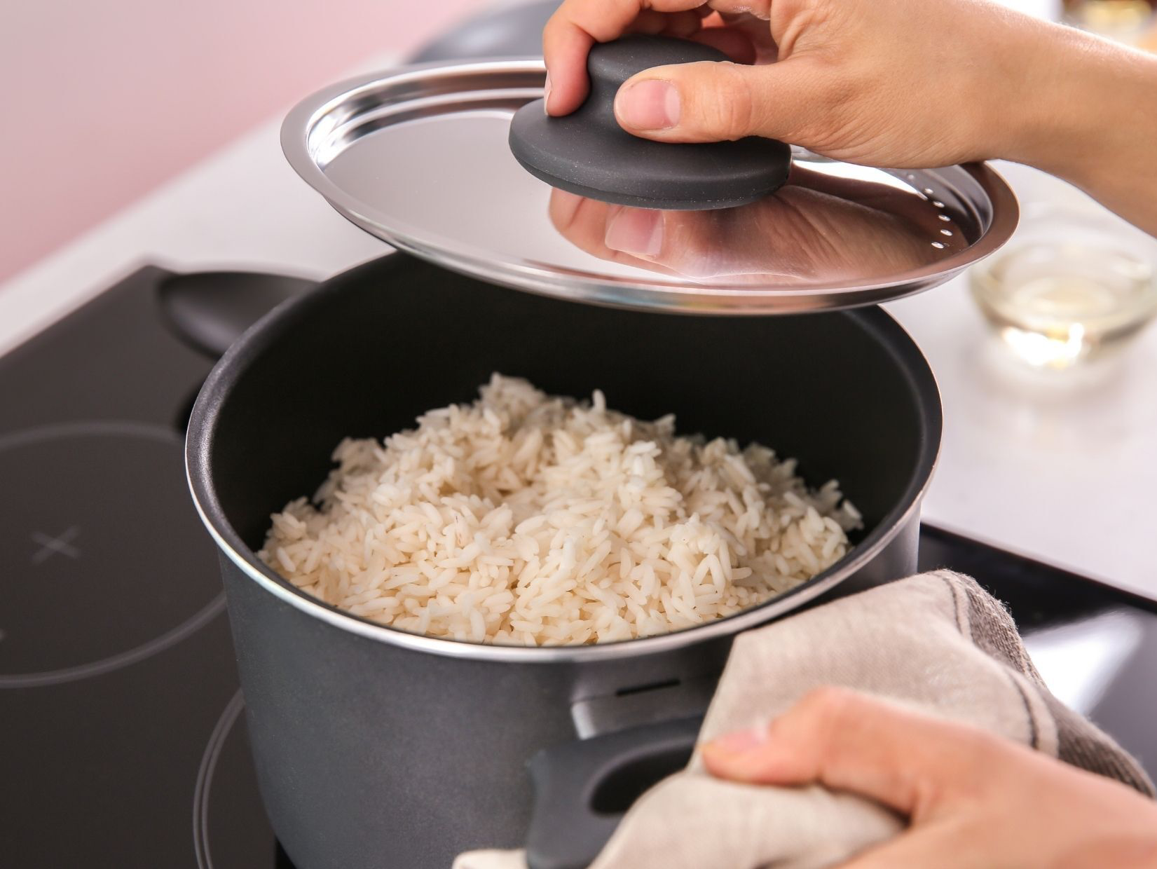 Person lifting lid off pot of cooked rice on stovetop.