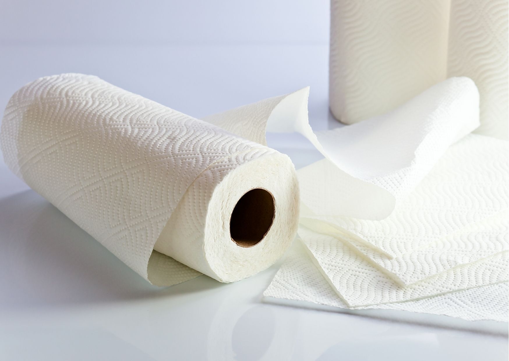 Paper towel roll partially unrolled on a white surface, with other rolls in the background.