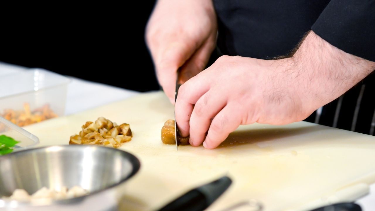 Chef slicing food on a cutting board, close-up shot.