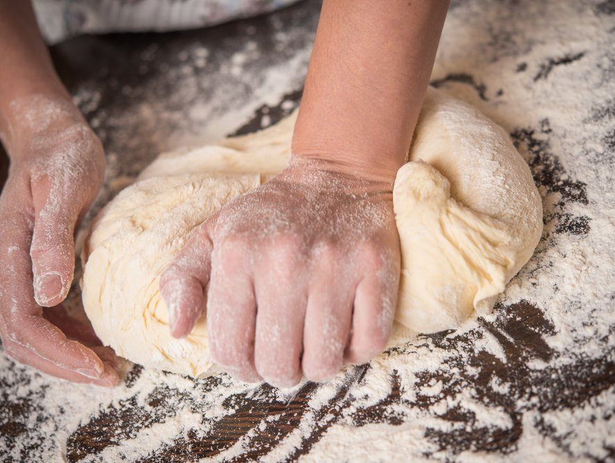 Hands kneading dough on a flour-dusted surface.