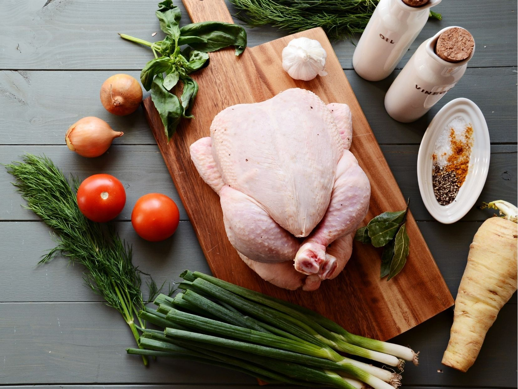 Raw chicken on cutting board with vegetables and spices.