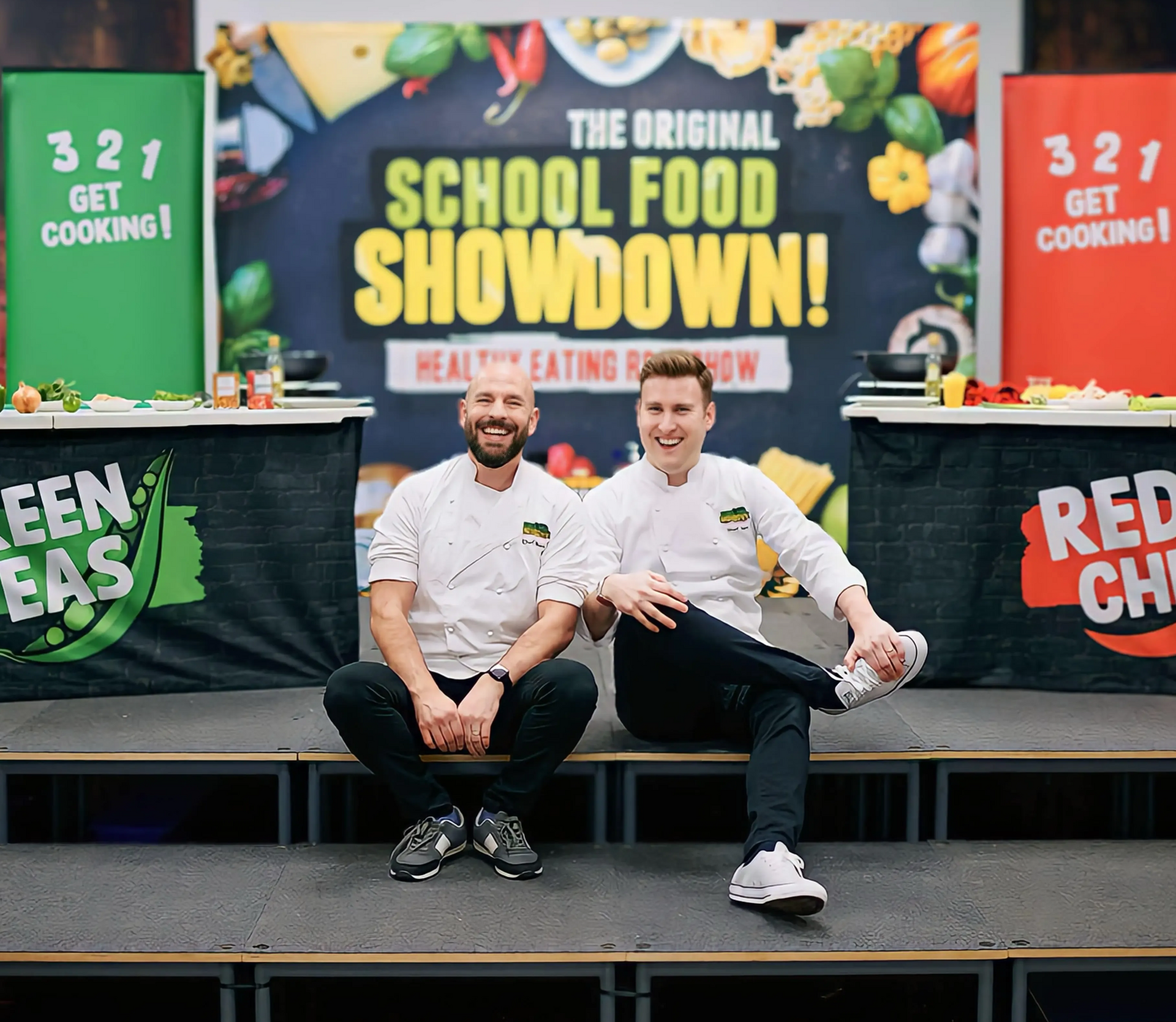 Two chefs sit on stage, smiling in front of
