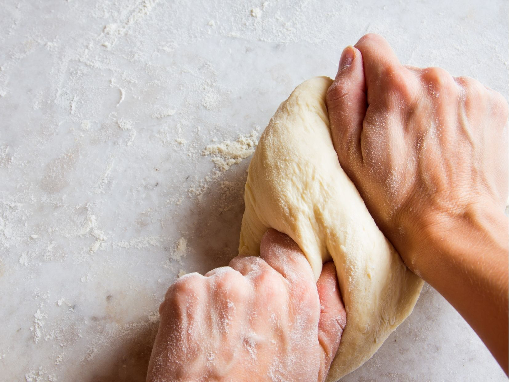 Hands kneading dough on a floured surface.