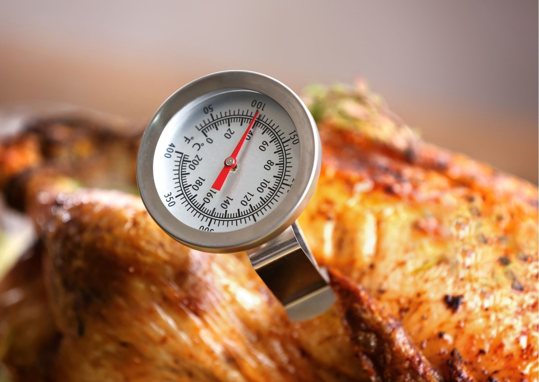 Meat thermometer inserted into roasted chicken, measuring internal temperature.