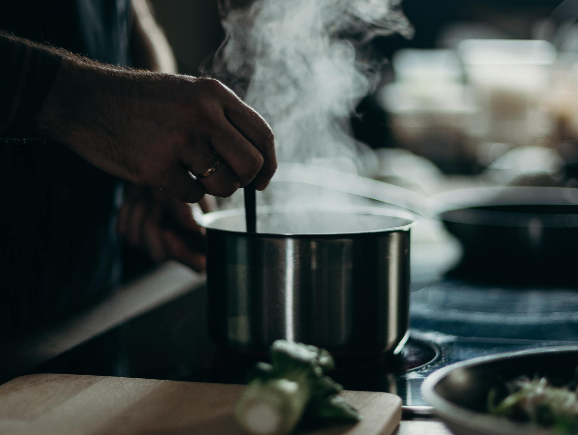 Person stirring steaming pot on stove in kitchen.