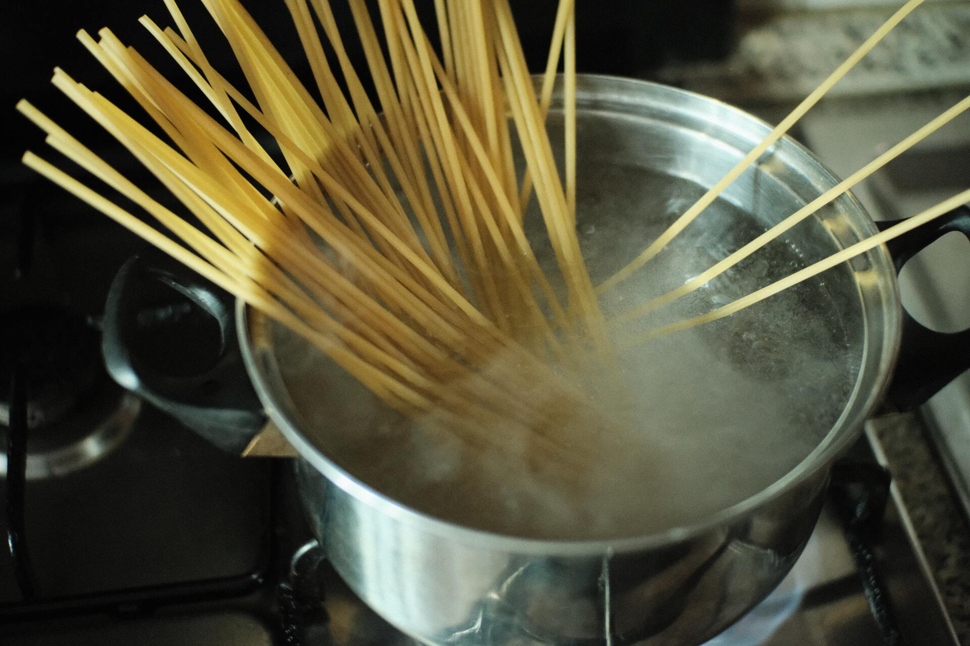 Spaghetti noodles being cooked in boiling water in a silver pot on a stove.