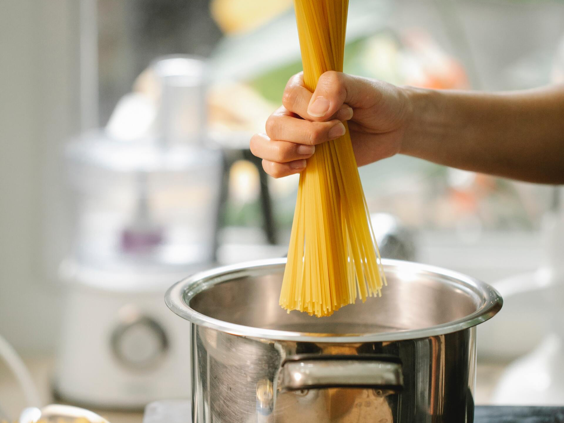Hand placing spaghetti into a pot of boiling water in a kitchen.