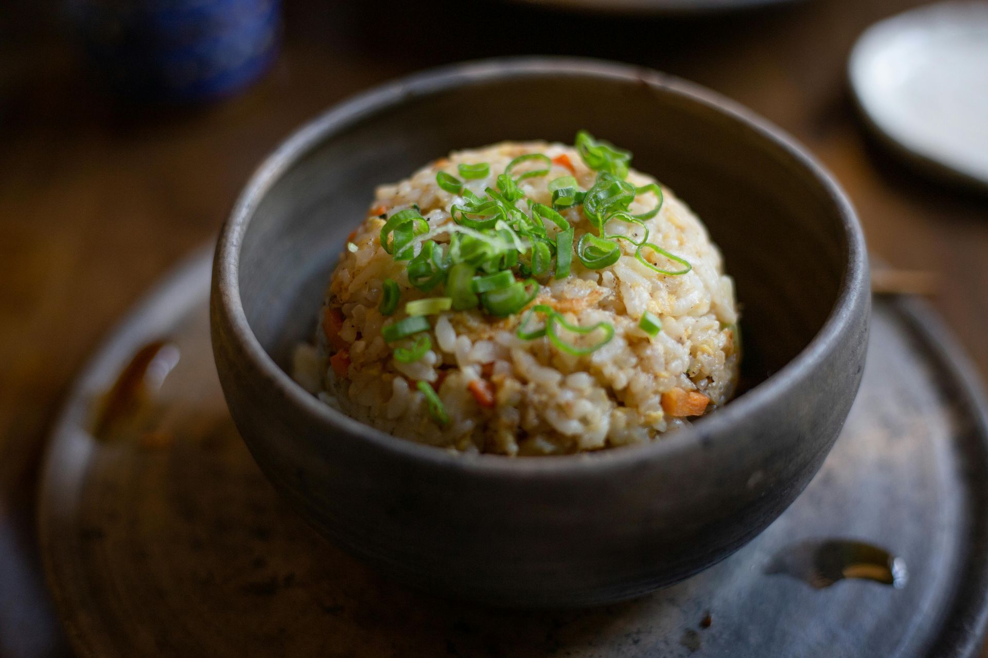 Rice dish in a dark bowl, garnished with chopped green onions, on a rustic plate.