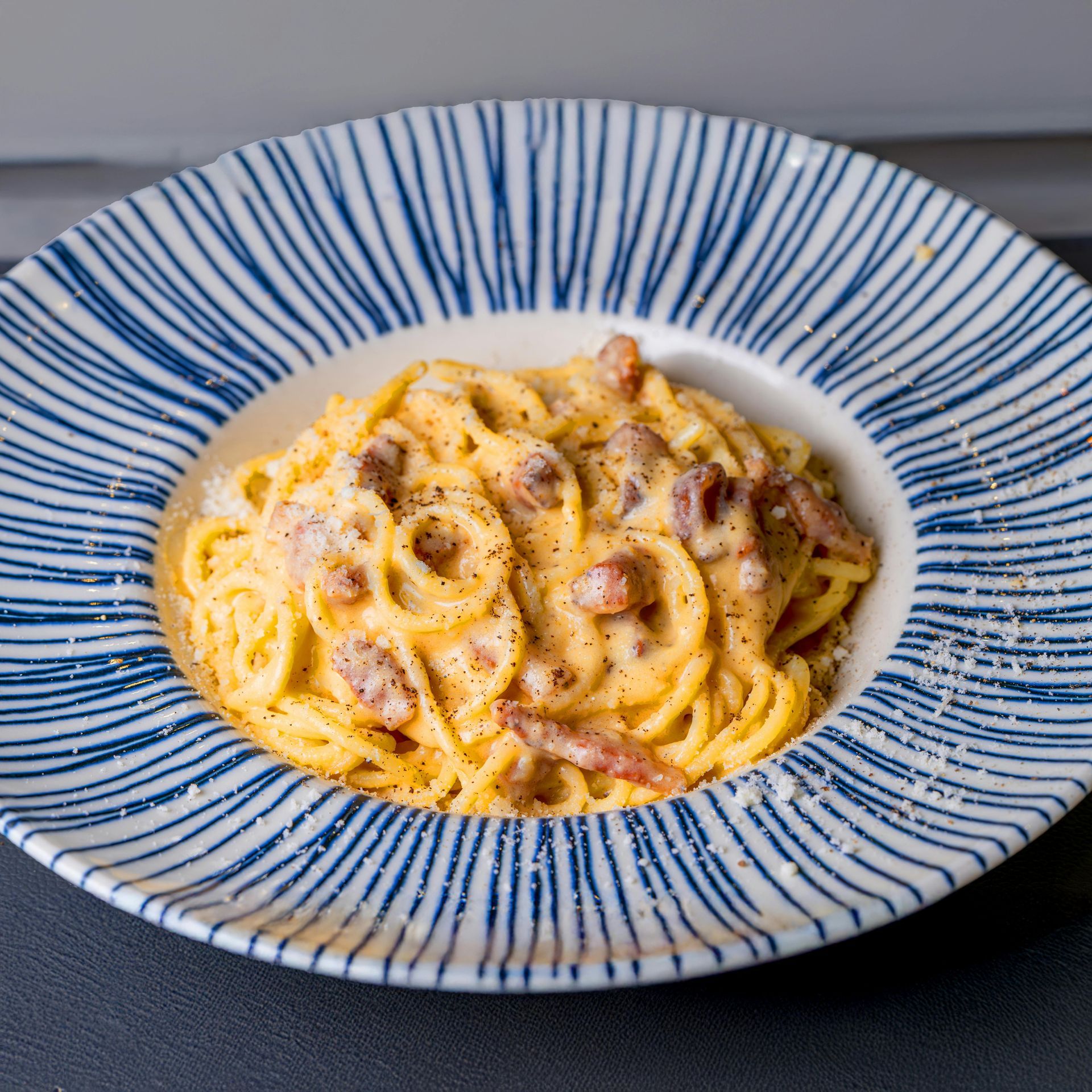 Creamy spaghetti carbonara in a blue-rimmed bowl on a dark table