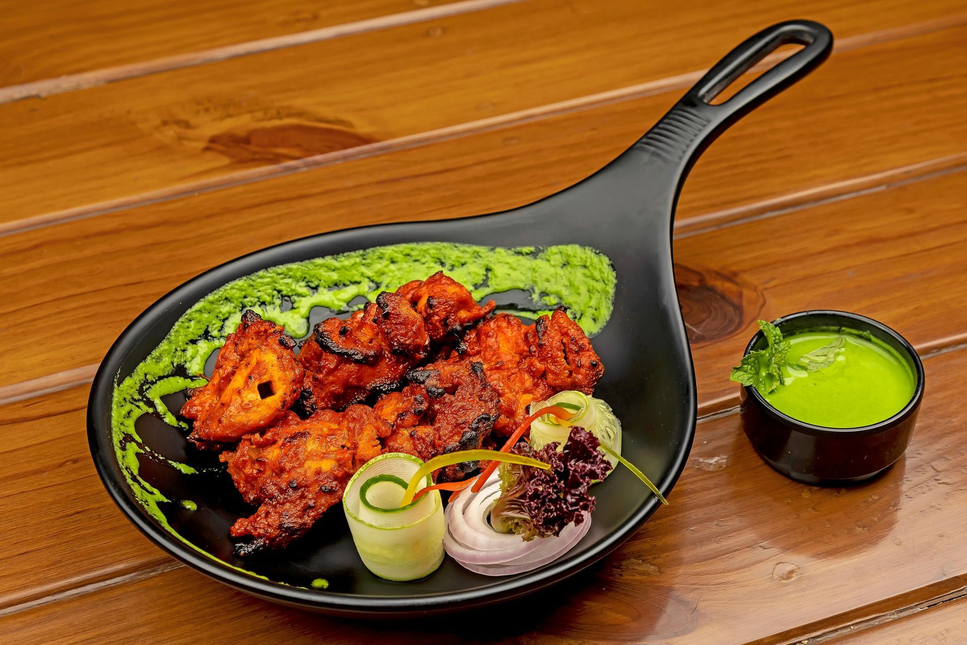 Black skillet with red grilled chicken, rice, and green sauce on a wooden table