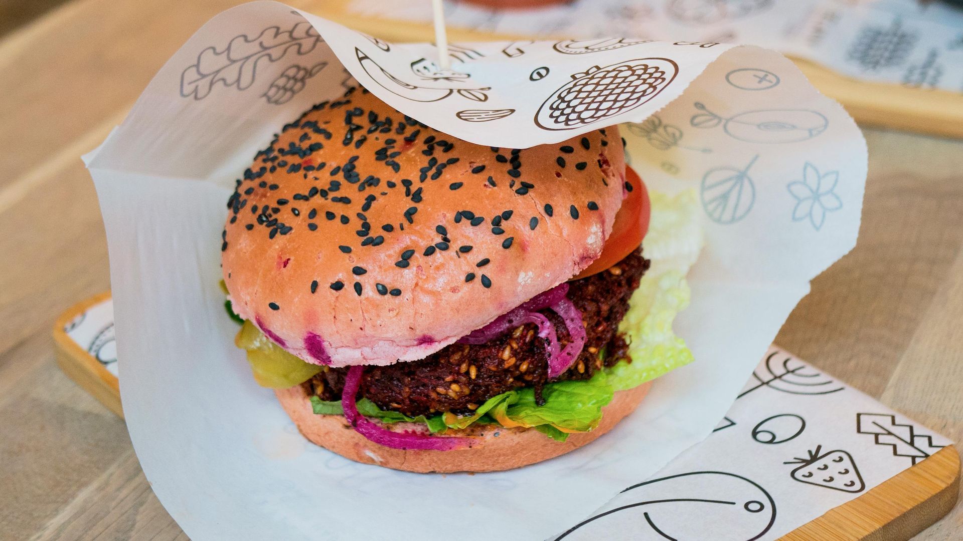 Sesame seed burger in paper wrapper, with lettuce, red onion, and purple slaw on a tray