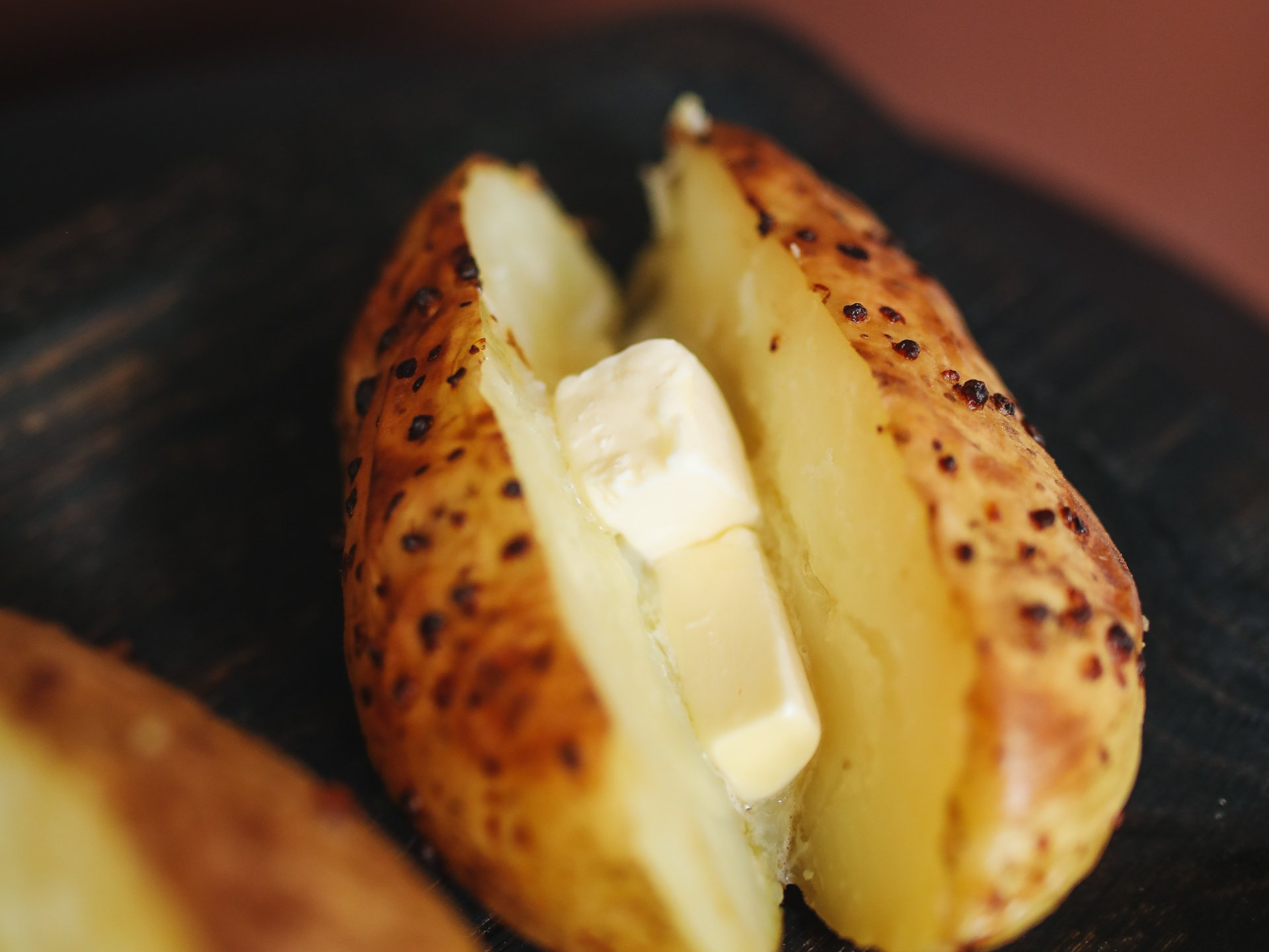 Baked potato, split open, with melting butter inside. Dark, wooden background.