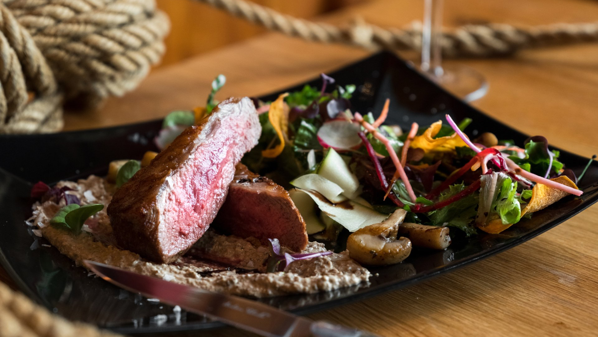 Sliced steak with salad and mushrooms on a black plate, wooden table background.