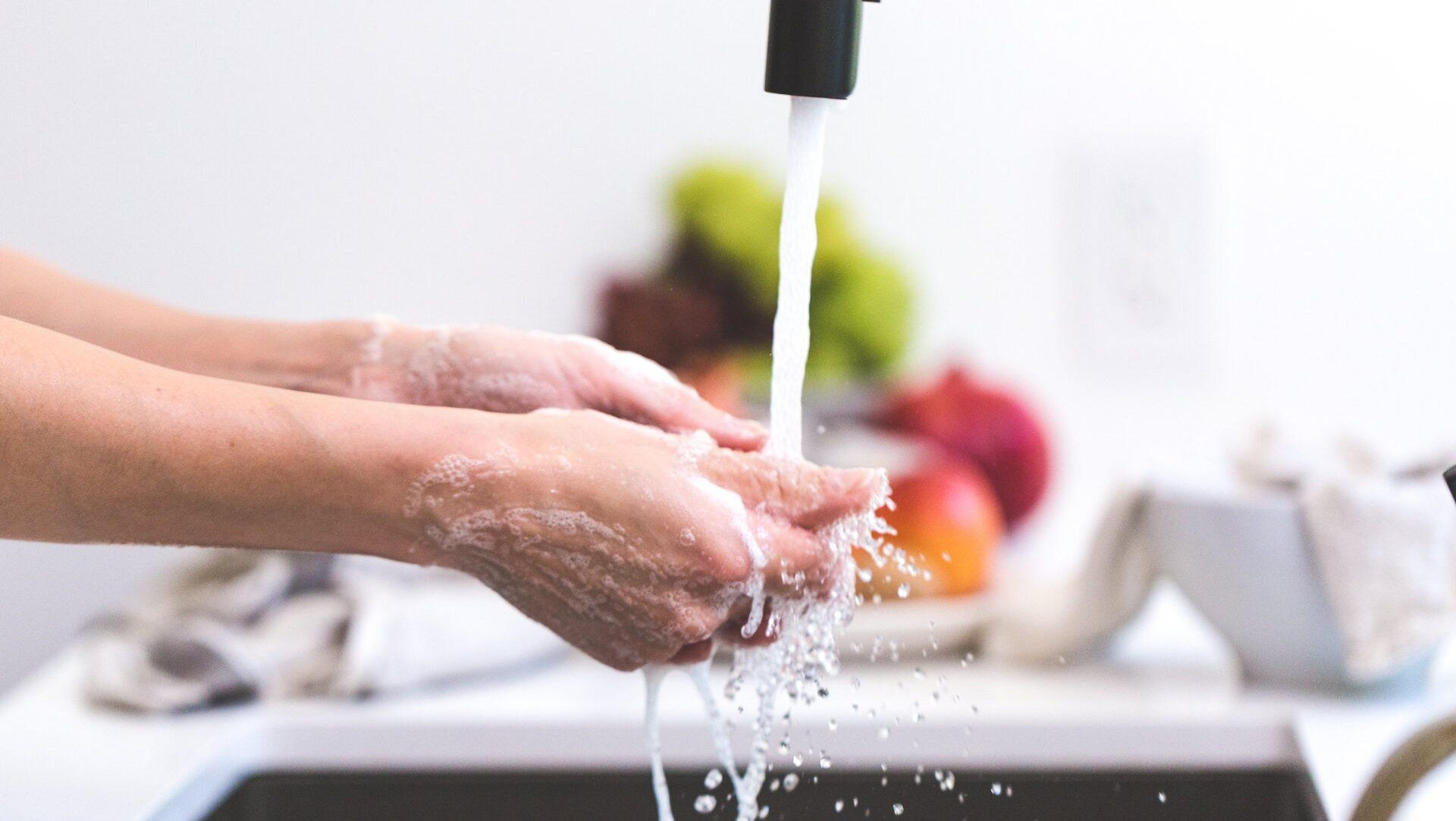 Hands being washed with soap under running water in a kitchen sink.