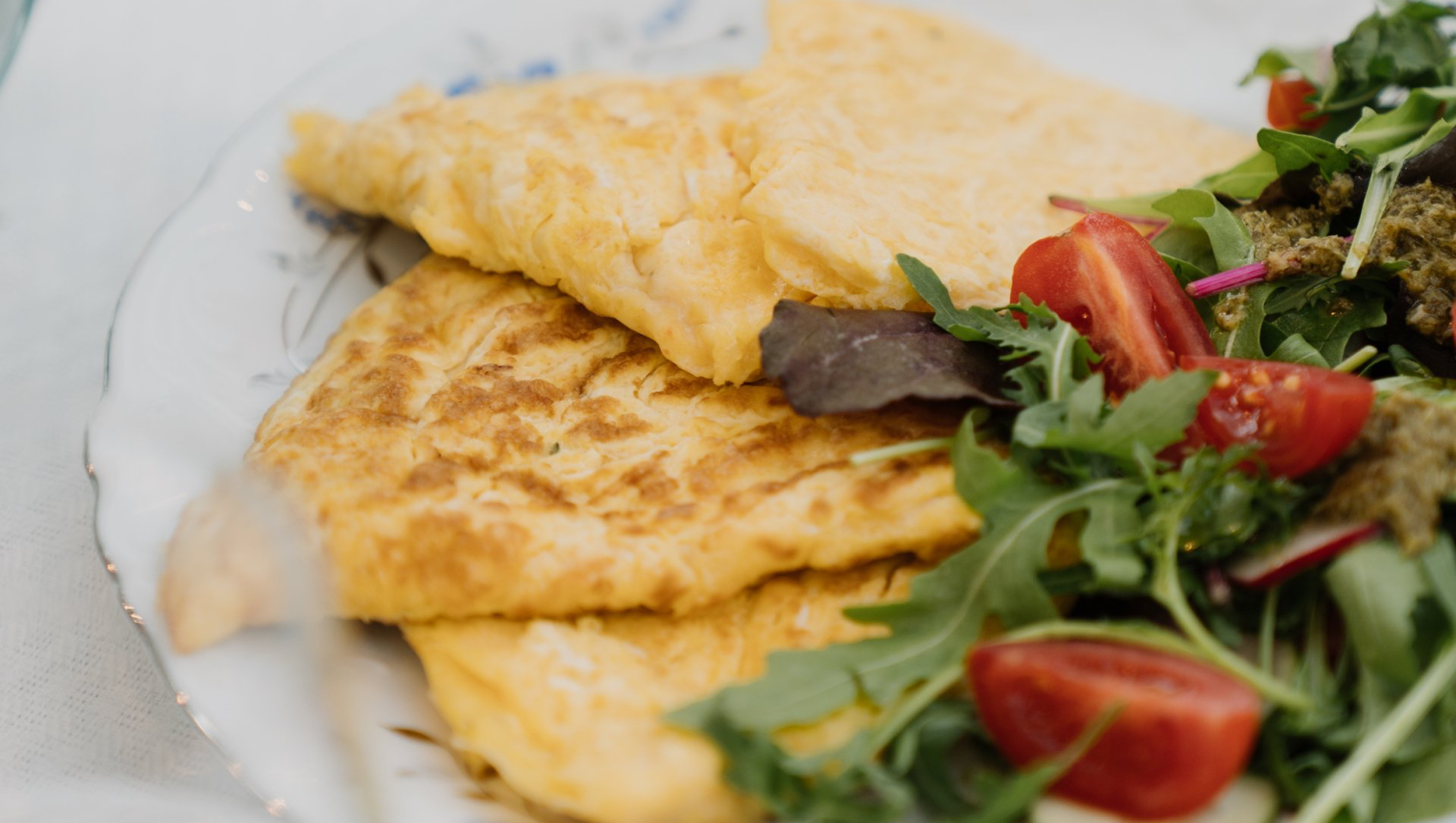 Omelet and salad on a plate. The omelet is golden, and the salad has arugula and tomatoes.