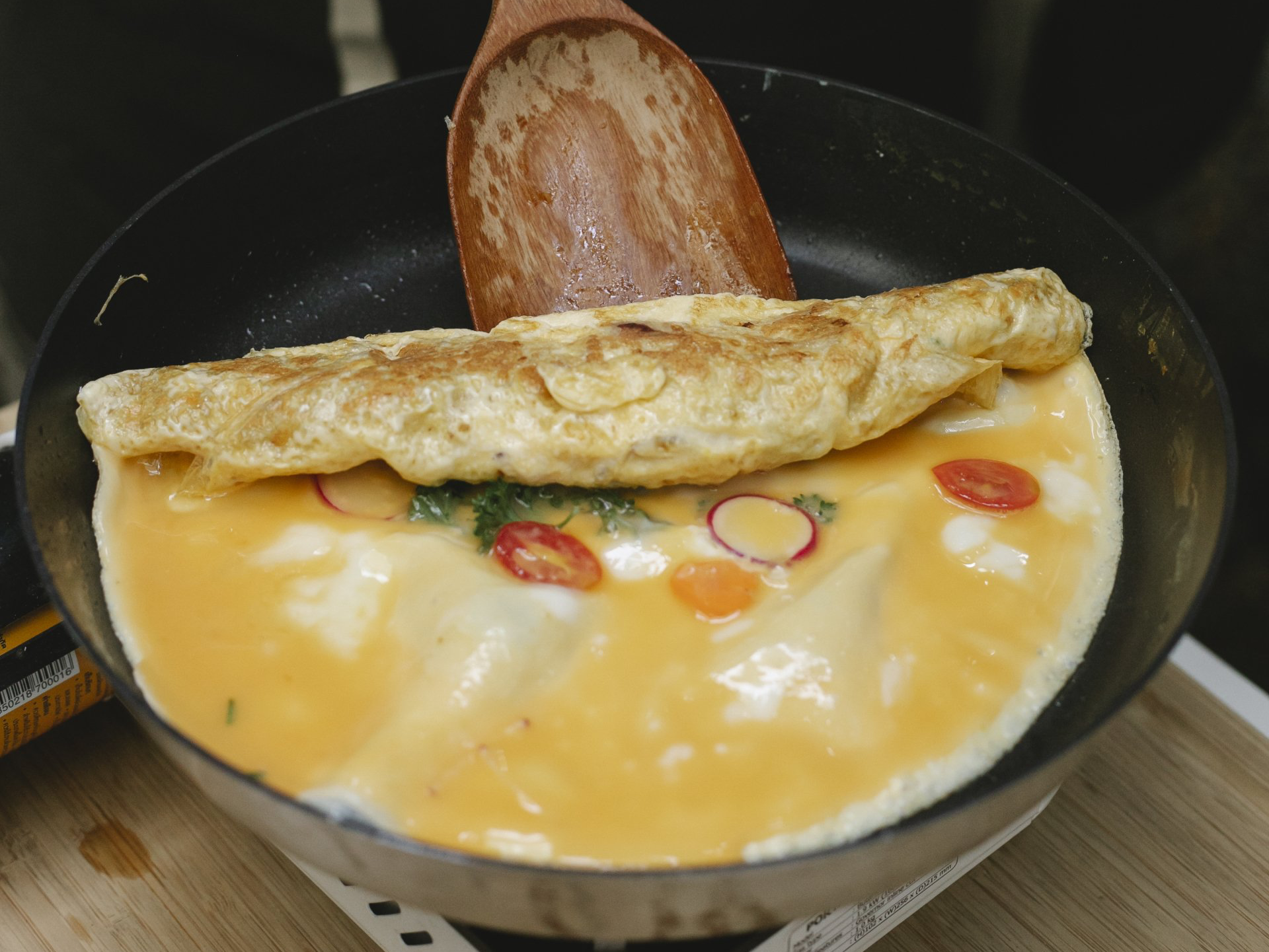 Omelette in a pan with veggies being folded with a wooden spatula.