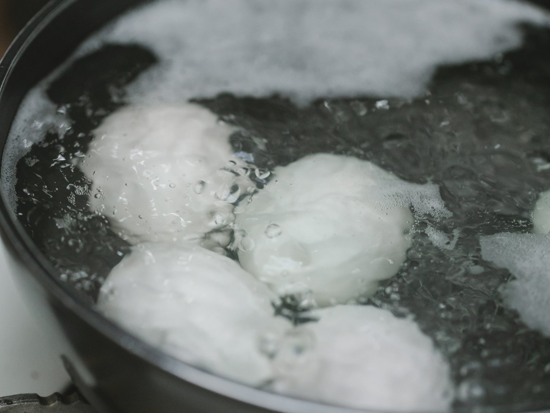 Eggs boiling in a pot of water, creating bubbles and steam.
