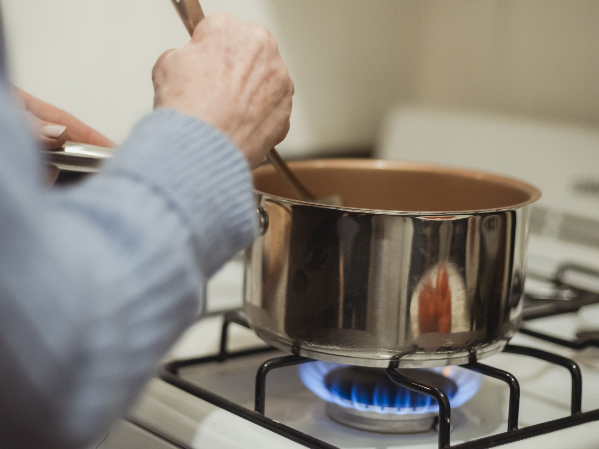 Person stirring pot on a gas stove with blue flames.
