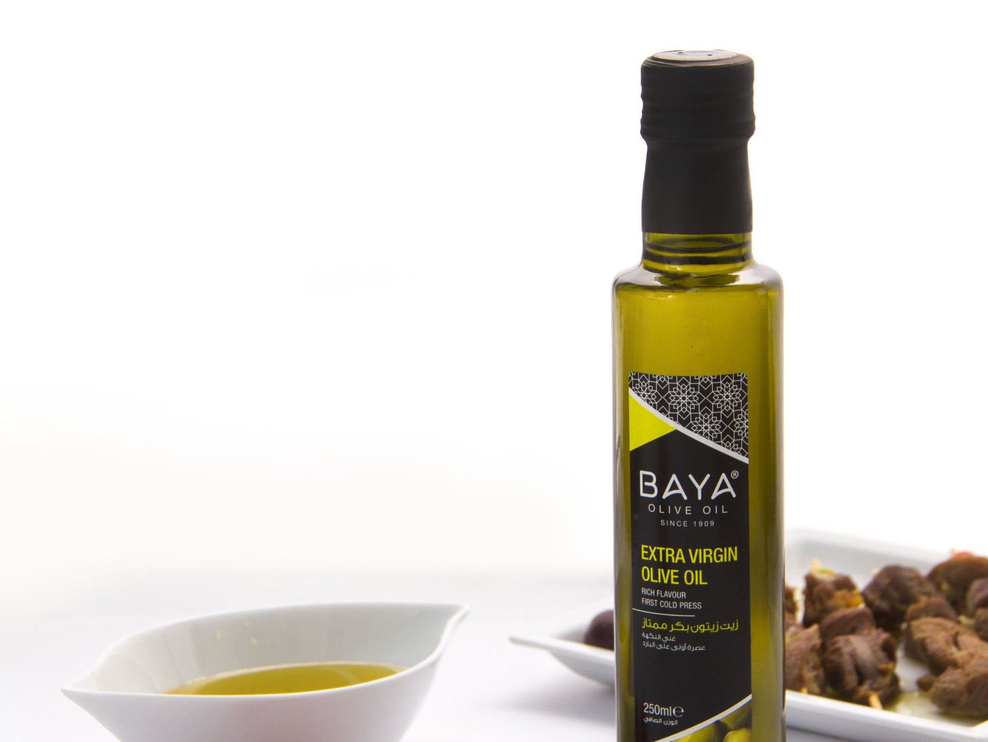 Olive oil bottle, white bowl with oil, olives, and food on a plate.