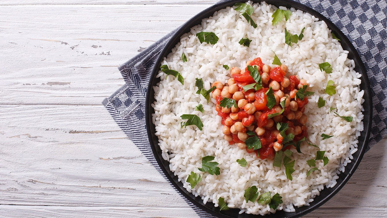 Rice dish topped with chickpeas and tomatoes, garnished with cilantro on a dark plate.