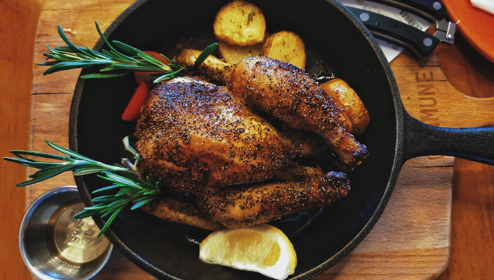 Roasted chicken with potatoes in a cast iron skillet, garnished with rosemary and lemon.