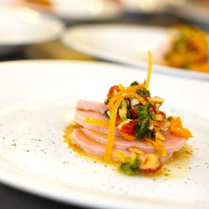Sliced pink fish topped with a colorful relish on a white plate.