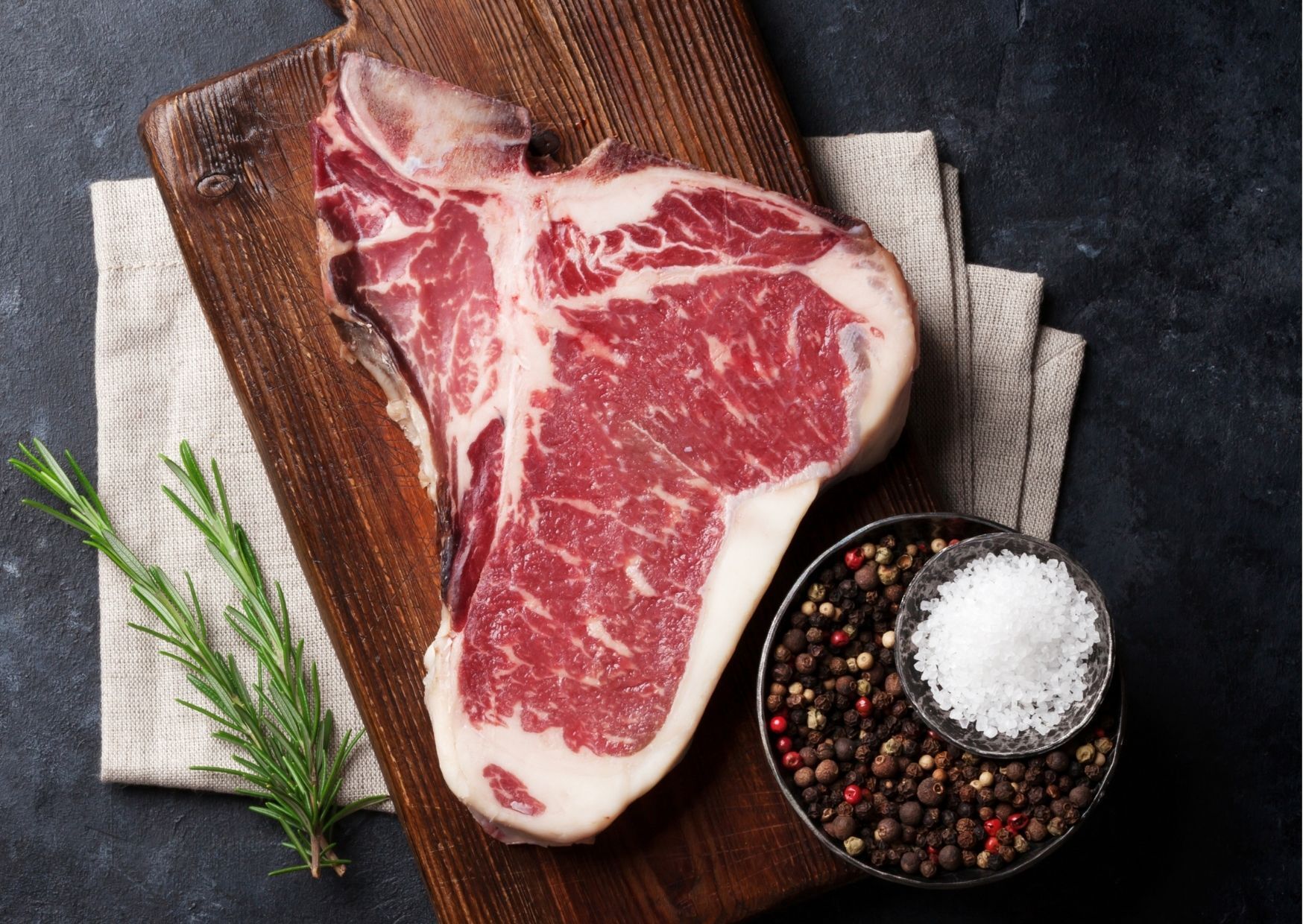T-bone steak on a wooden board with salt, pepper, and rosemary.
