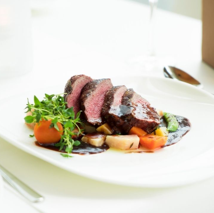 Sliced steak with vegetables and sauce on a white plate.