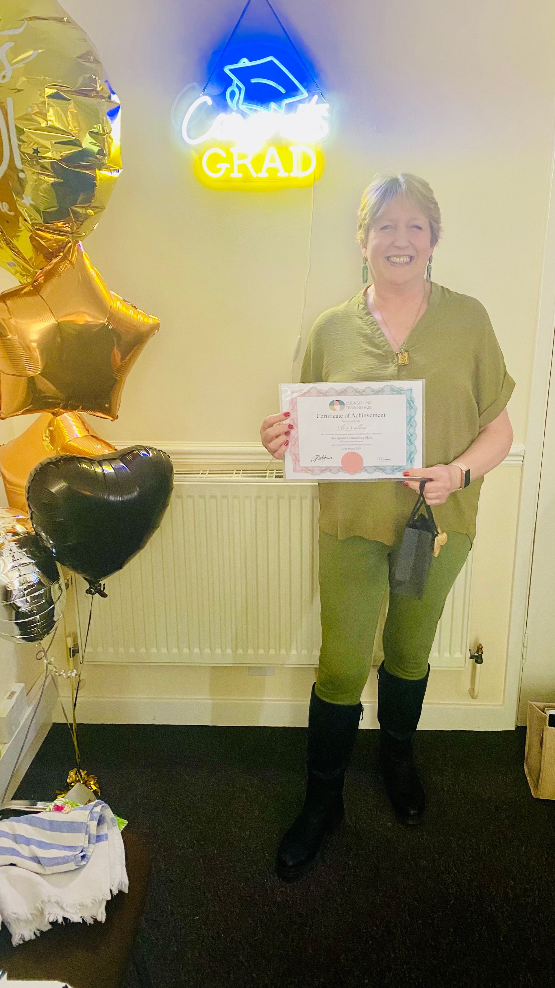 Woman in green holding certificate, standing next to balloons, under a 