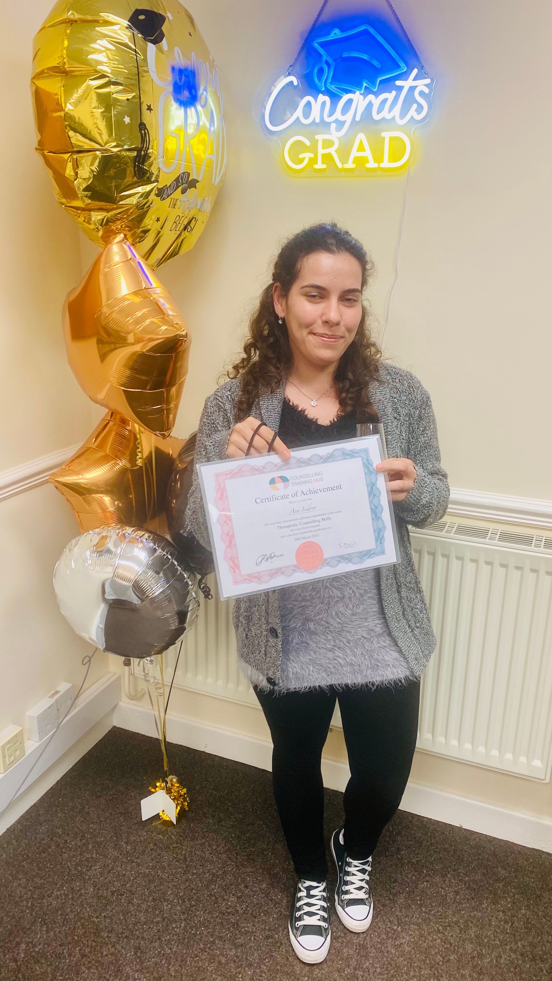 Woman holding a diploma, smiling, standing by balloons and a 