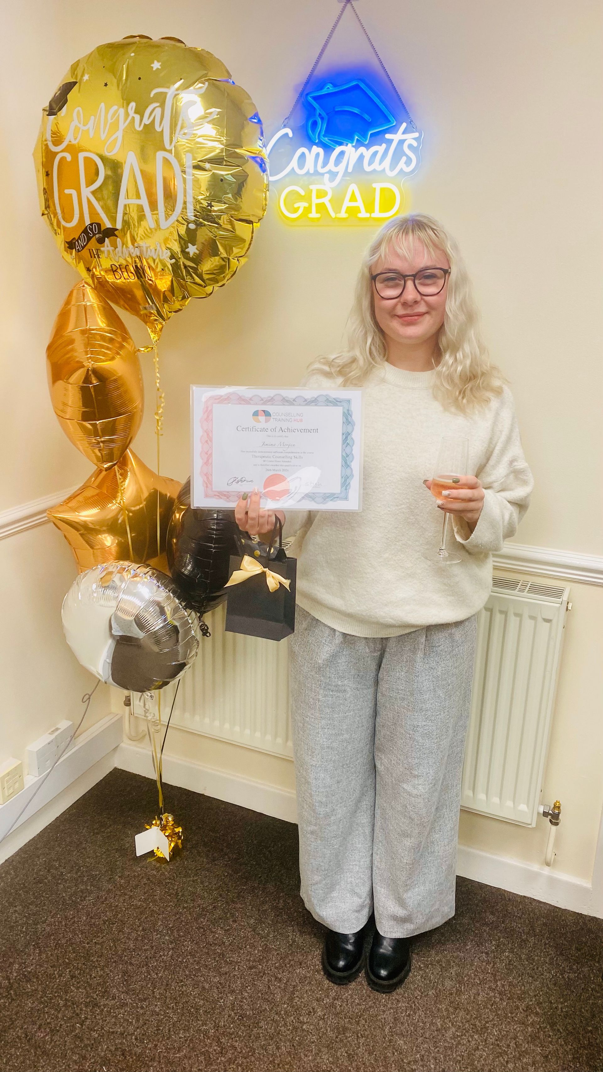 Woman holding a certificate, celebrating graduation with balloons and a neon sign.