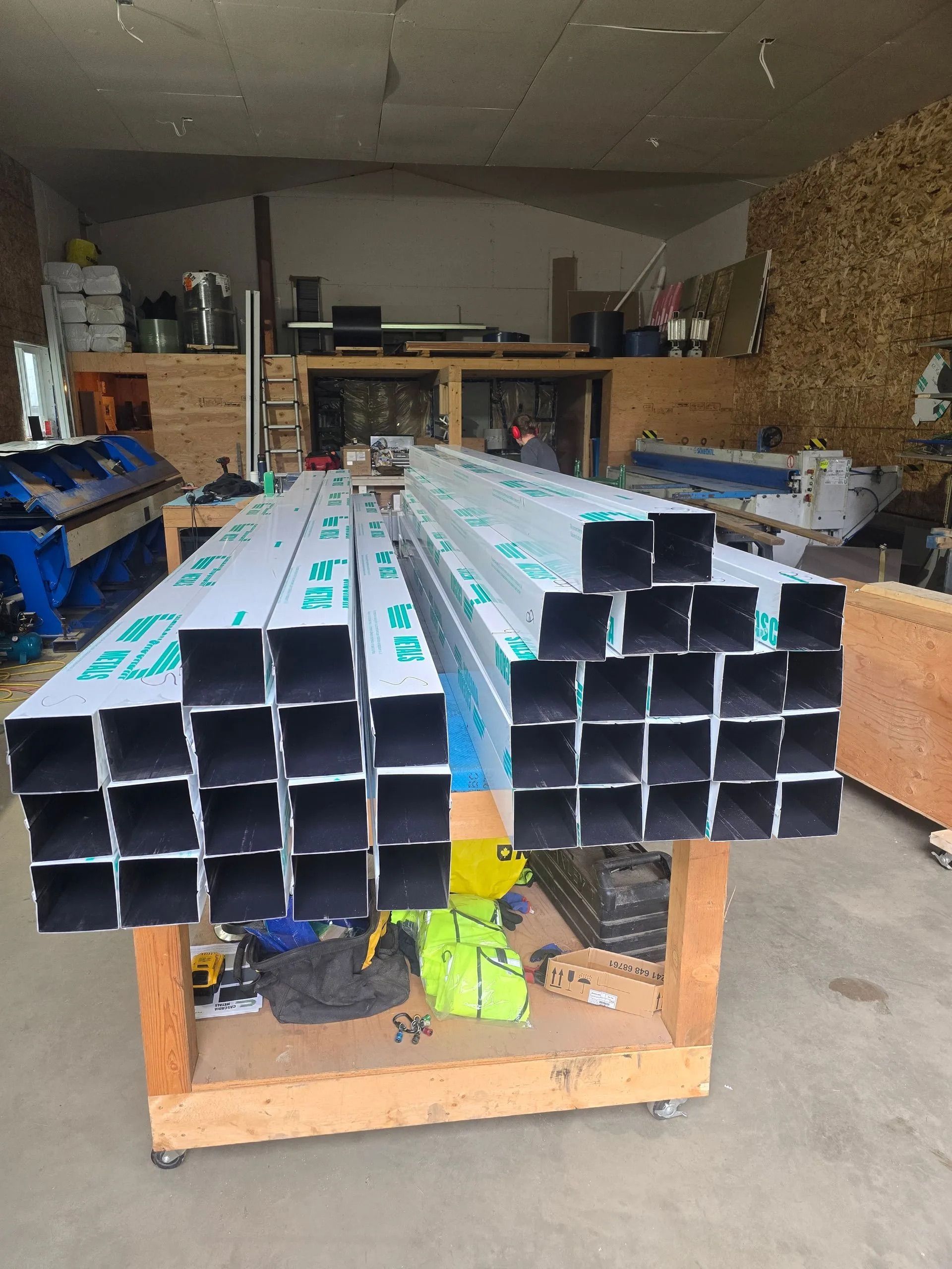 Stacked metal pipes on a cart in a workshop, with black ends and turquoise labels on top.