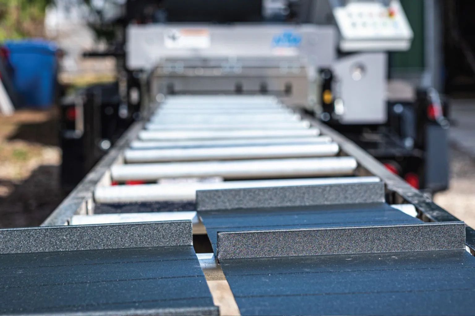 Close-up of a conveyor machine with metal rollers and dark rubber belts in an industrial setting