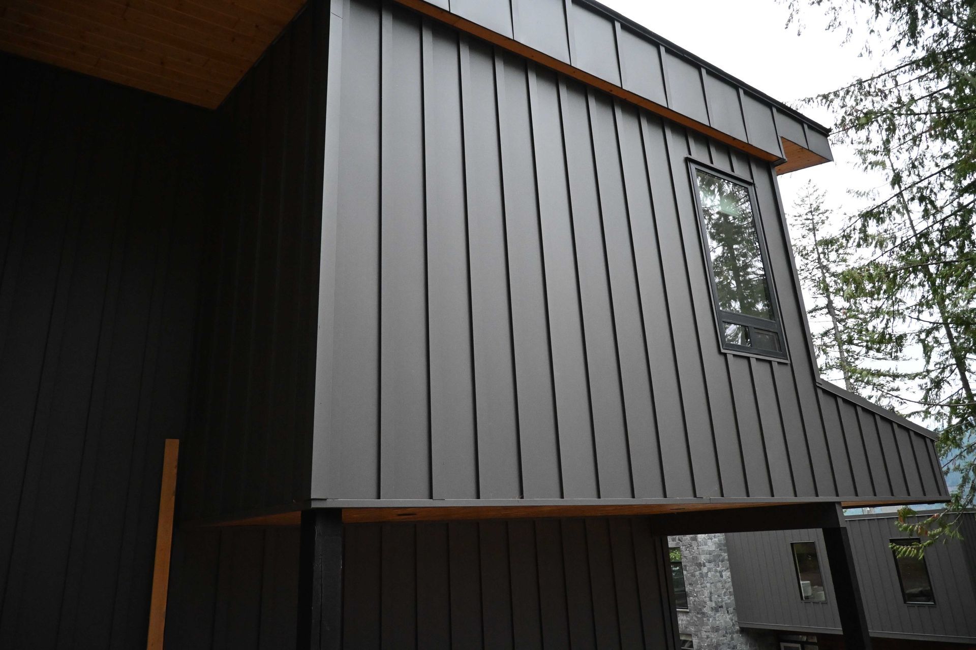 Modern dark wood house exterior with vertical paneling and a small window under an overhanging roof