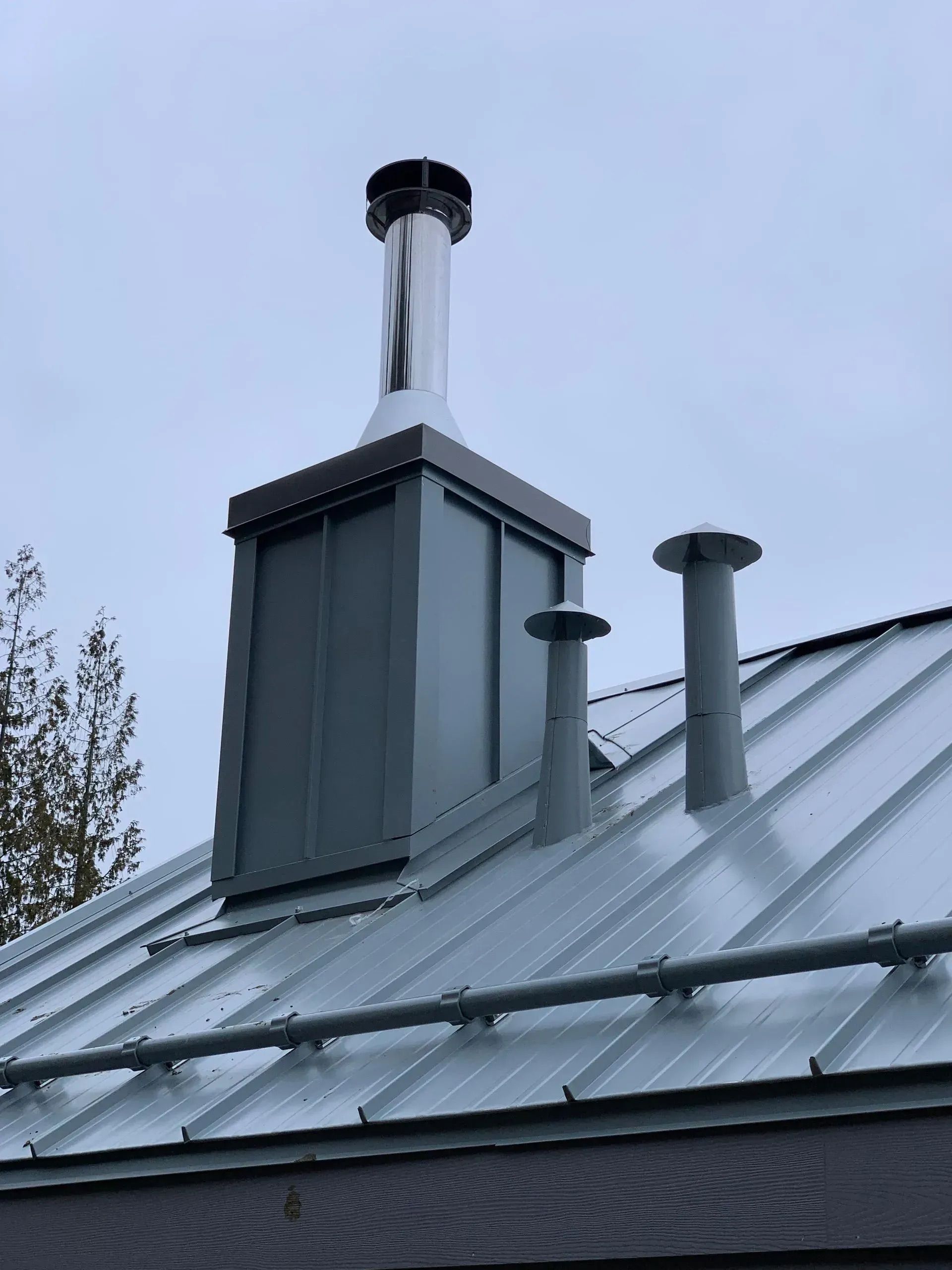 Snowy metal rooftop with chimney vents and a central roof chimney under a cloudy sky