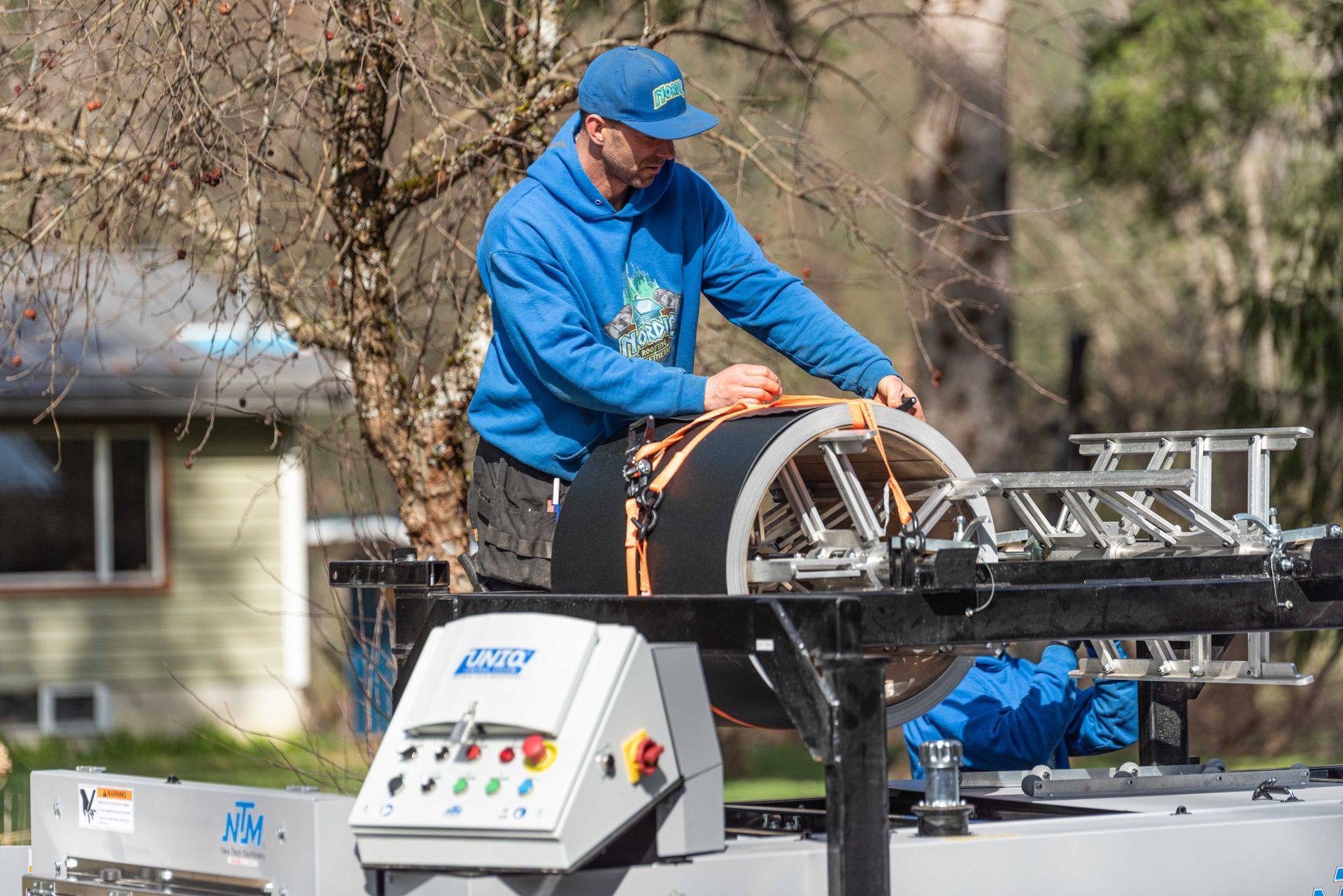 Worker in blue jacket operating rooftop equipment on a truck-mounted platform outdoors