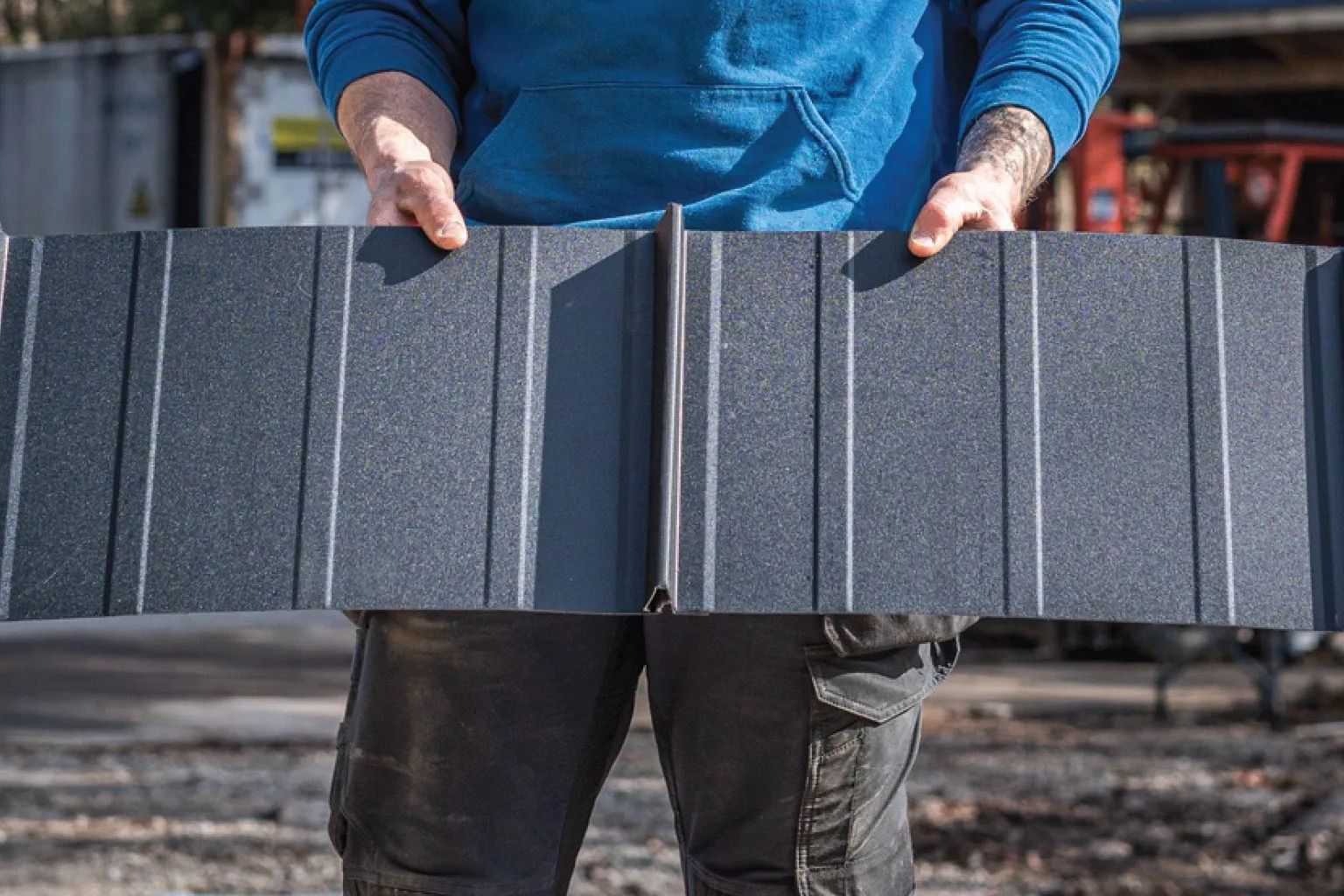 Person holding a long gray metal panel outdoors on a construction site