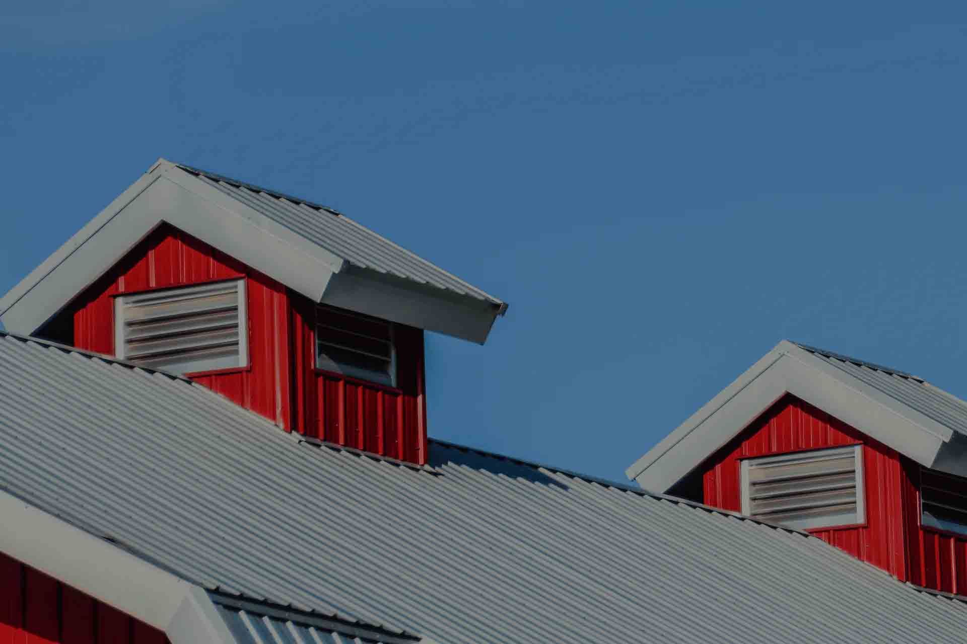 Red barn rooftops with gray metal roofs against a clear blue sky