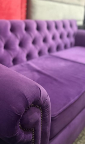 Sofá capitoné de terciopelo morado con brazos enrollados y ribete de tachuelas.